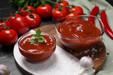 Organic ketchup in bowls and ingredients on black table. Tomato sauce