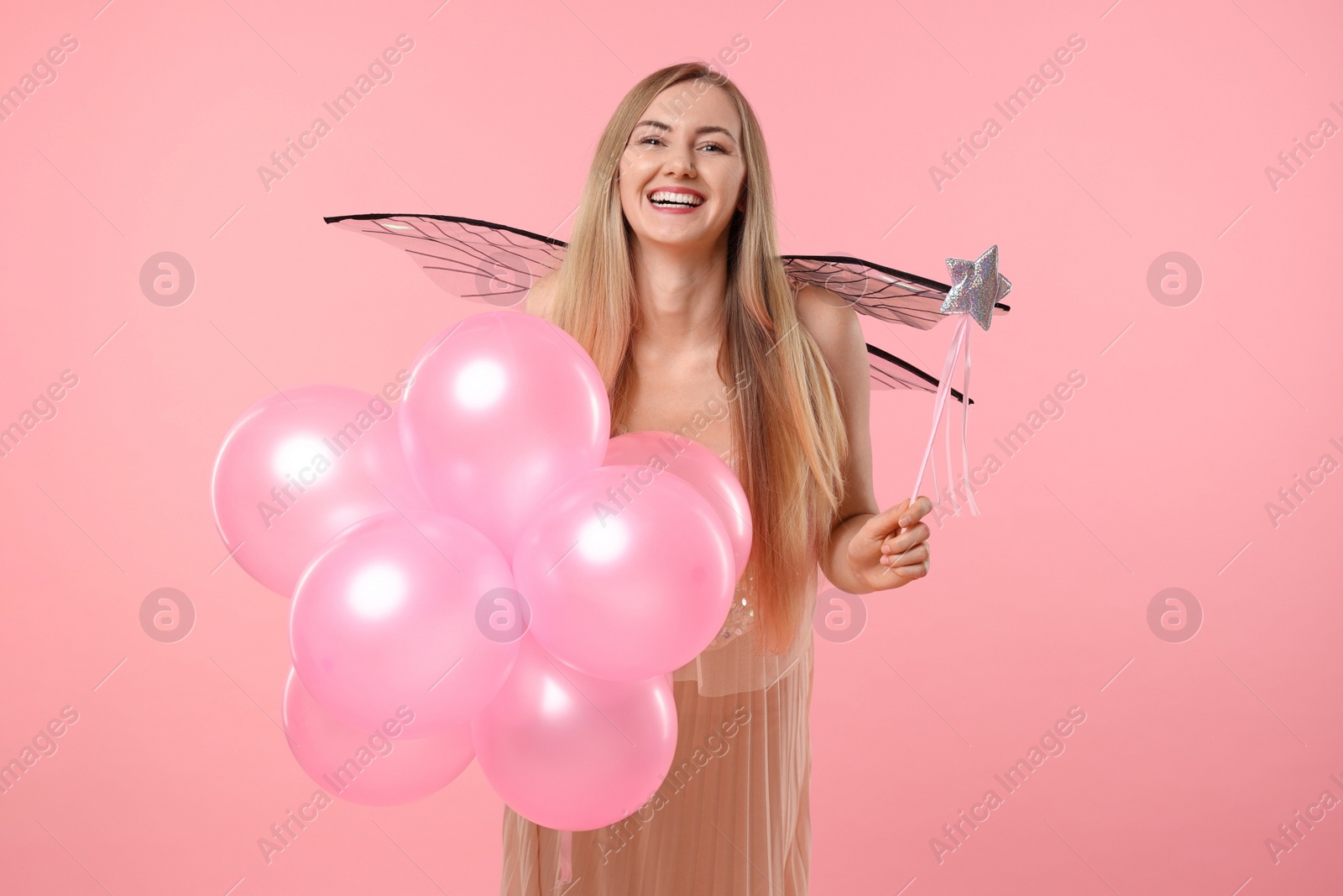 Photo of Beautiful girl in fairy costume with wings, magic wand and balloons on pink background