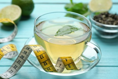 Photo of Cup of herbal diet tea and measuring tape on light blue wooden table