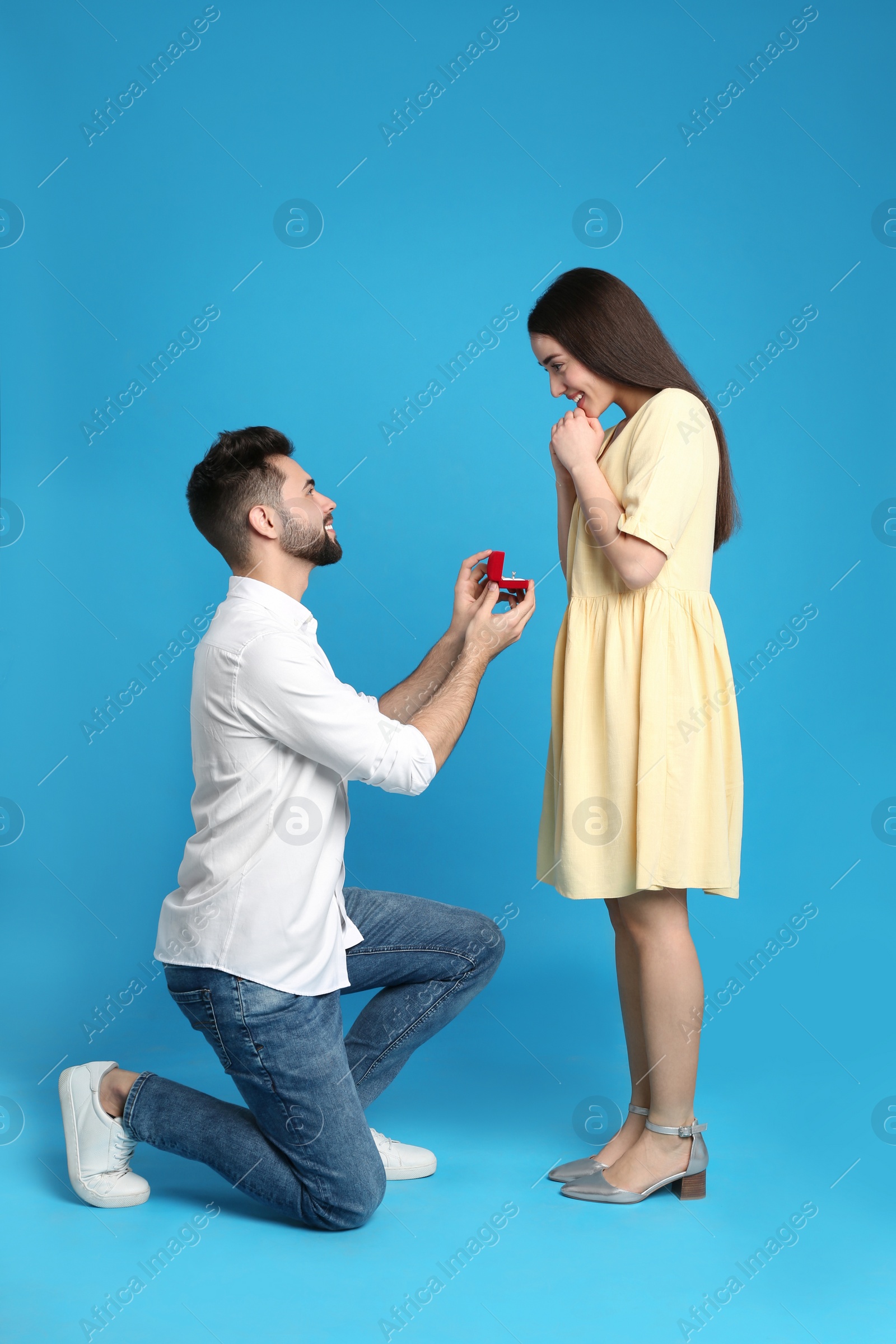 Photo of Man with engagement ring making marriage proposal to girlfriend on blue background