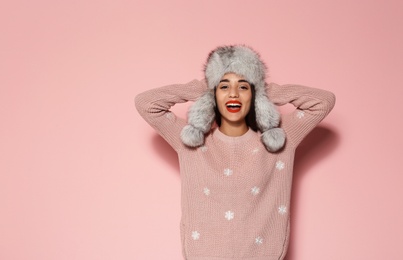 Young woman in warm sweater and hat on color background. Celebrating Christmas