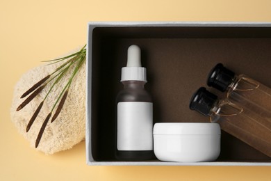 Photo of Box with cosmetic products, rolled towel and reeds on beige background, flat lay