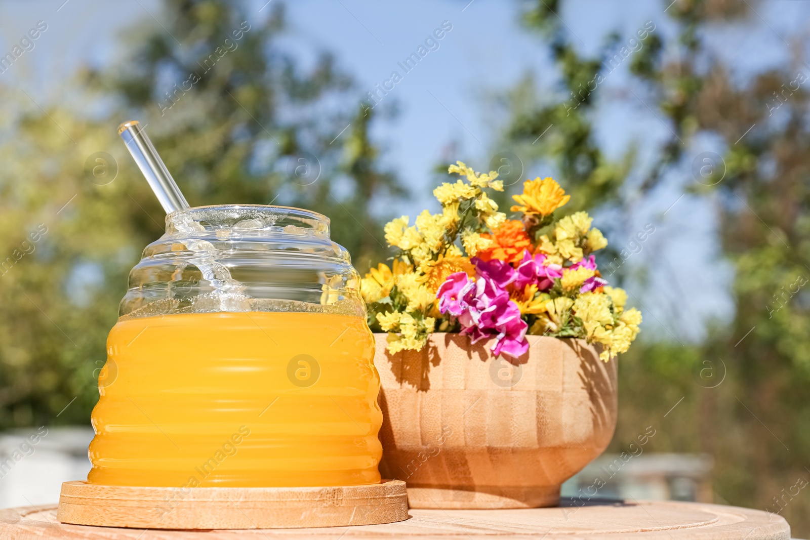 Photo of Delicious fresh honey and beautiful flowers on wooden board in apiary