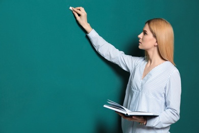 Beautiful teacher with book writing on chalkboard, space for text