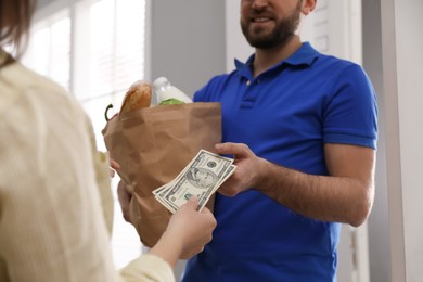 Photo of Young woman giving tips to courier indoors, closeup