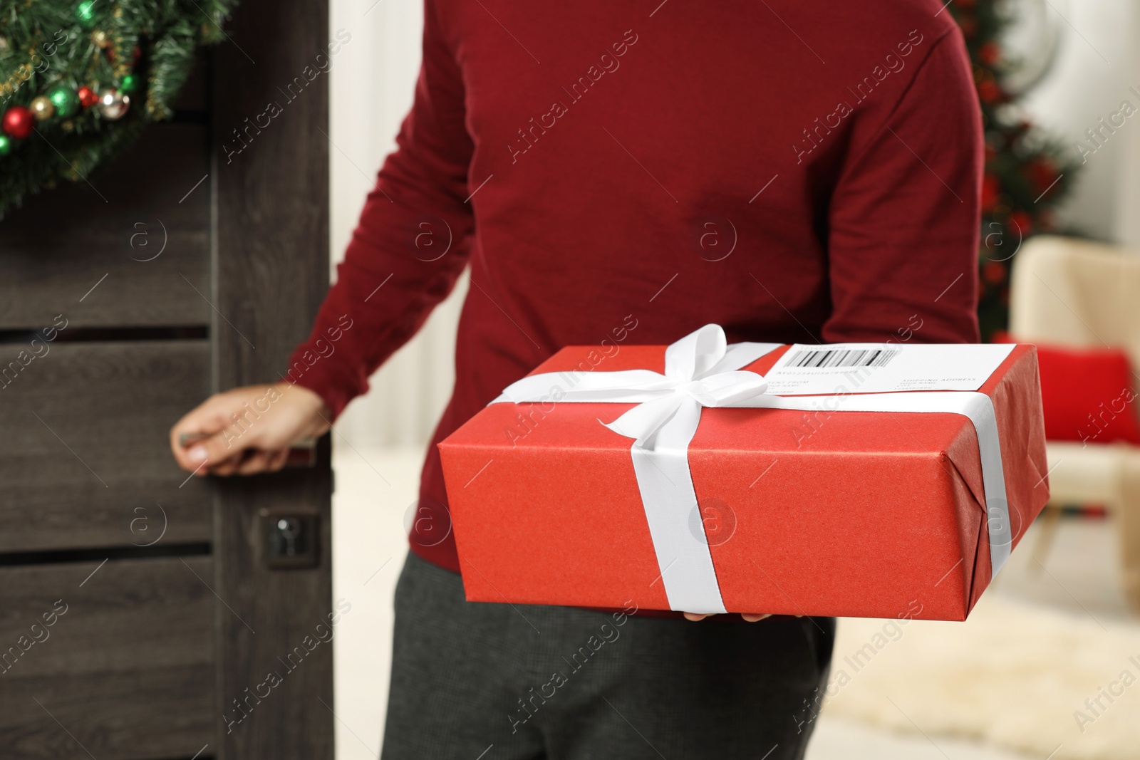 Photo of Young man in Santa hat with Christmas gift box received by mail indoors, closeup