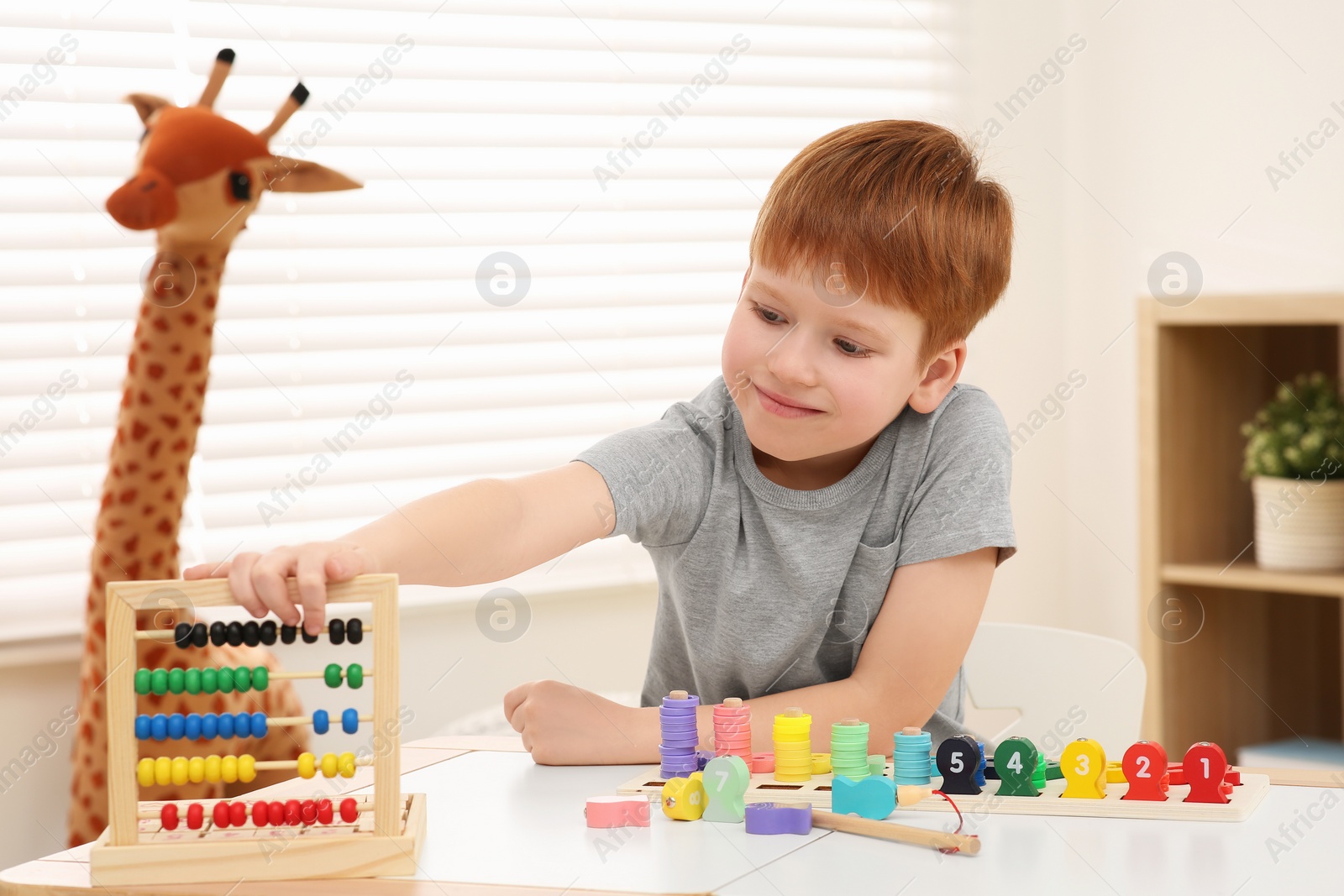 Photo of Happy little boy playing with abacus at desk in room. Learning mathematics with fun