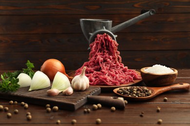 Photo of Meat grinder with beef mince, onion, parsley, garlic and spices on wooden table