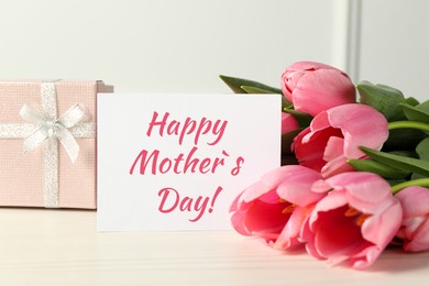 Happy Mother's Day greeting card, gift box and beautiful tulips on white wooden table