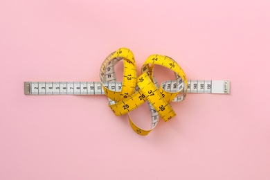 Measuring tape on pink background, top view