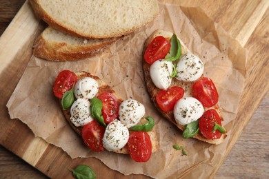 Photo of Delicious sandwiches with mozzarella, fresh tomatoes and basil on wooden board, top view