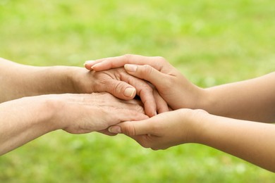 Photo of Young and elderly women holding hands outdoors, closeup