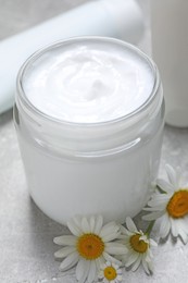 Photo of Jar of hand cream and chamomiles on light grey table, closeup