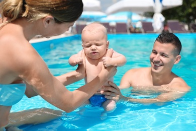 Happy parents with little baby in swimming pool on sunny day, outdoors