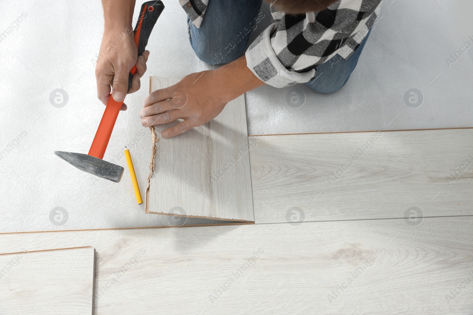 Photo of Professional worker using hammer during installation of new laminate flooring, above view