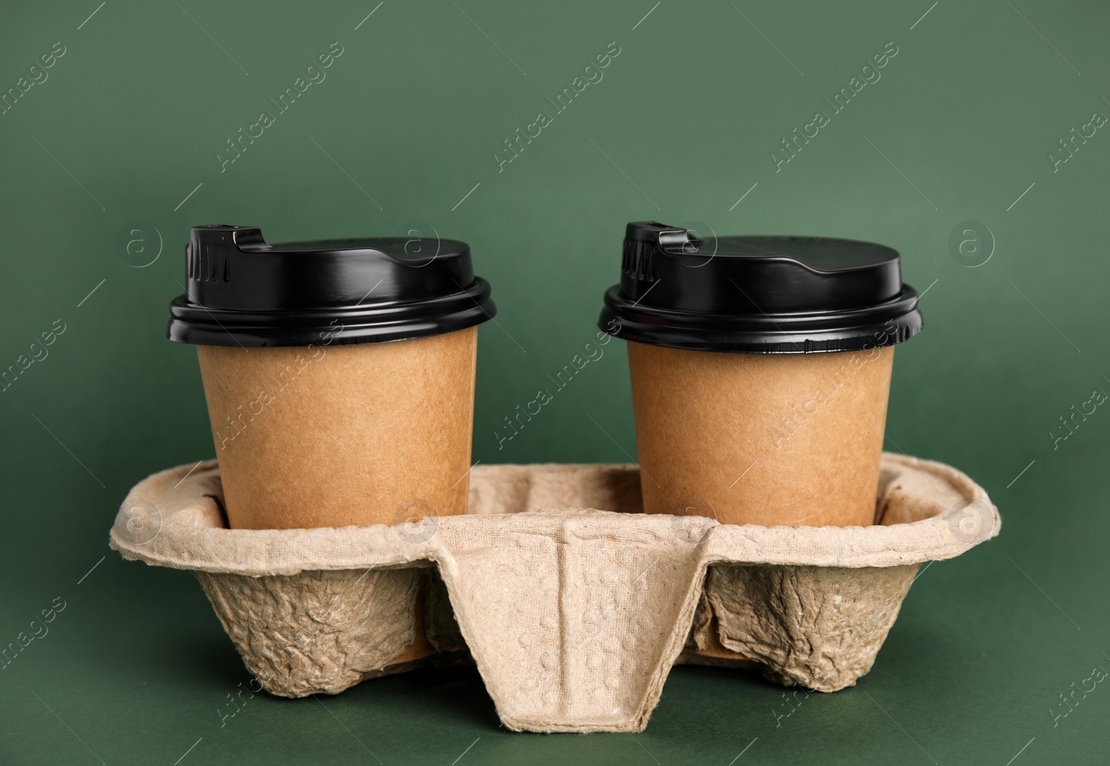 Photo of Takeaway paper coffee cups with plastic lids in cardboard holder on dark green background