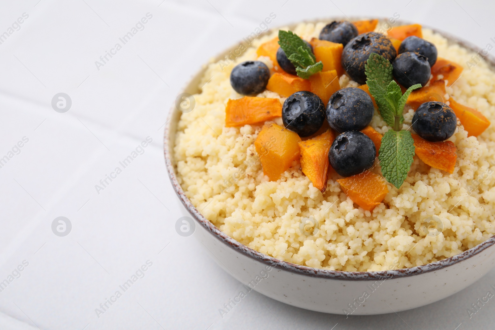 Photo of Bowl of tasty couscous with blueberries, pumpkin and mint on white table, closeup. Space for text