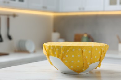 Photo of Bowl covered with beeswax food wrap on white table indoors, space for text