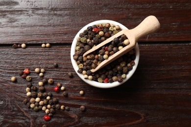 Photo of Aromatic spice. Different peppers in bowl and scoop on wooden table, top view