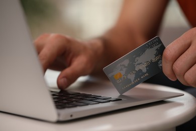 Photo of Man using laptop and credit card for online payment at table indoors, closeup