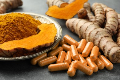 Photo of Aromatic turmeric powder, pills and raw roots on grey table, closeup
