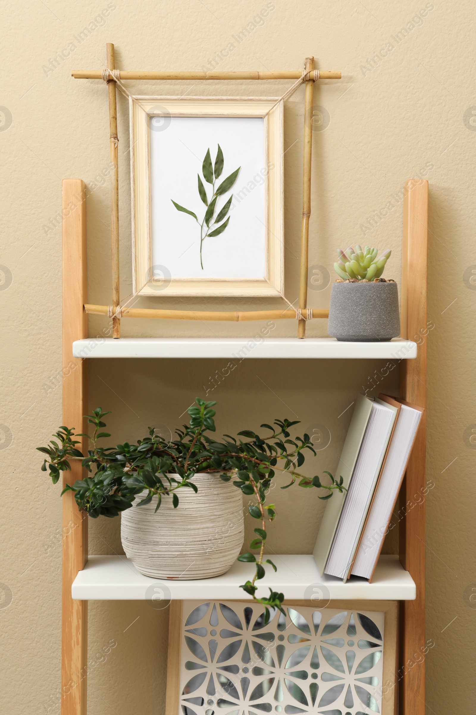 Photo of Bamboo frame and different decor elements on shelving unit near beige wall