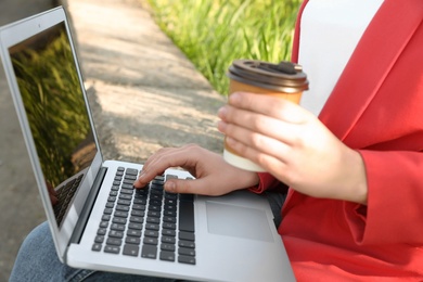 Image of Woman with paper cup of coffee using laptop outdoors, closeup
