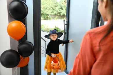 Cute little girl dressed as witch trick-or-treating at doorway. Halloween tradition