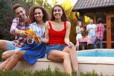 Photo of Happy friends with drinks at barbecue party near swimming pool outdoors