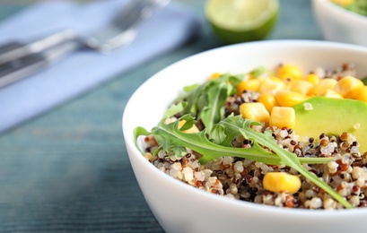Photo of Healthy quinoa salad with vegetables in bowl on wooden table. Space for text