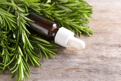 Photo of Bottle of rosemary essential oil on wooden background