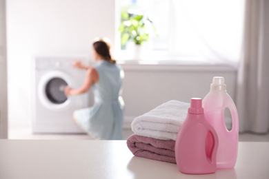 Photo of Stack of clean towels, detergents and blurred woman on background. Space for text