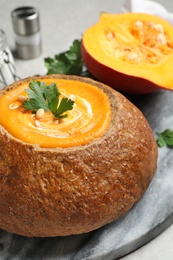 Photo of Tasty pumpkin cream soup in bread loaf on grey table