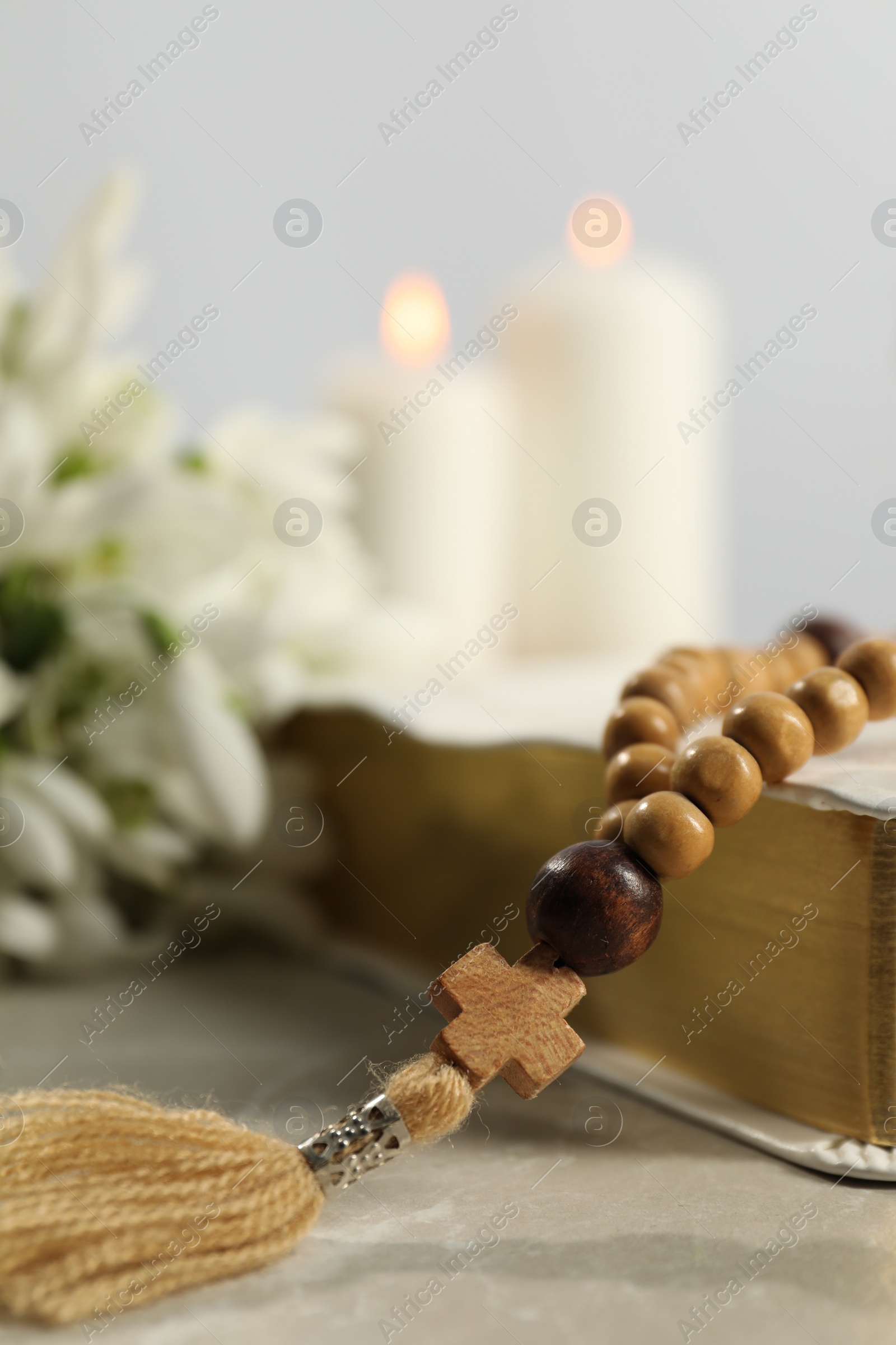 Photo of Bible, rosary beads and church candles on light table, closeup