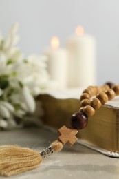 Photo of Bible, rosary beads and church candles on light table, closeup