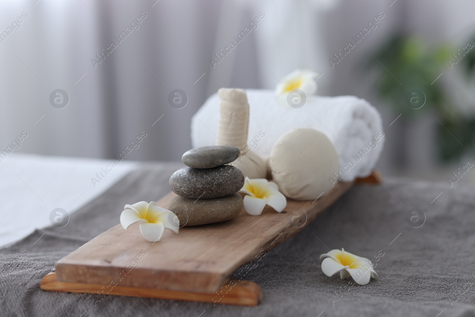 Photo of Stacked spa stones, flowers, herbal bags and towel on massage table indoors