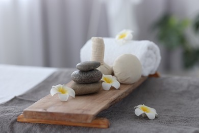 Photo of Stacked spa stones, flowers, herbal bags and towel on massage table indoors