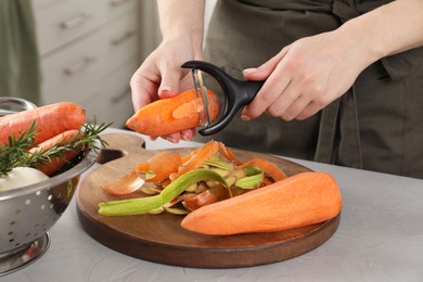 Photo of Woman peeling fresh carrot at light table indoors, closeup