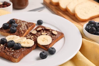 Photo of Toasts with tasty nut butter, banana slices, blueberries and hazelnuts on table, closeup