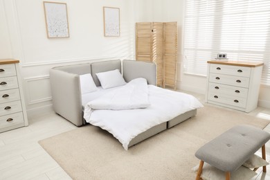 Photo of Stylish room interior with sleeper sofa near white wall. Additional place for guest