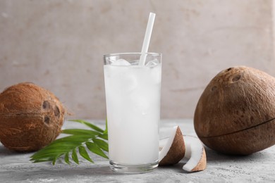 Photo of Glass of coconut water with ice cubes, palm leaf and nuts on grey table