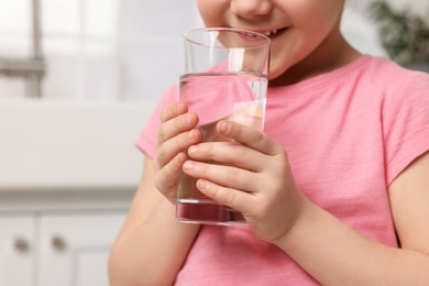 Photo of Little girl drinking fresh water from glass at home, closeup