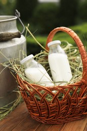 Photo of Tasty fresh milk in can and bottles on wooden table outdoors