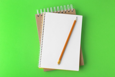 Photo of Notebooks with pencil on light green background, top view