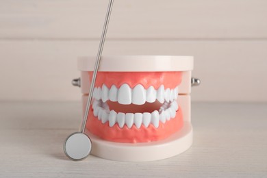 Photo of Model of jaw with teeth and dental mirror on white wooden table