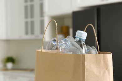 Paper bag with used plastic bottles in kitchen, closeup. Recycling problem