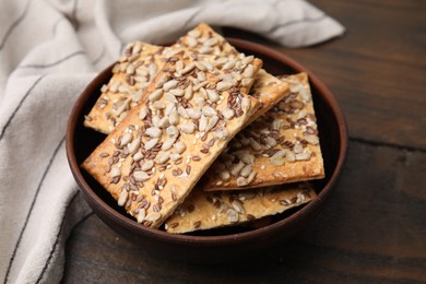Photo of Cereal crackers with flax, sunflower and sesame seeds in bowl on wooden table, closeup