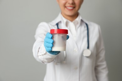 Photo of Doctor holding container with sperm on grey background, closeup