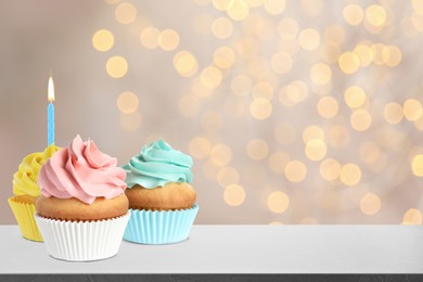 Image of Tasty birthday cupcakes on white table against blurred lights. Space for text