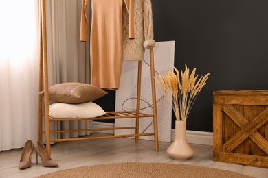 Photo of Dry plants near clothes rack indoors. Interior design